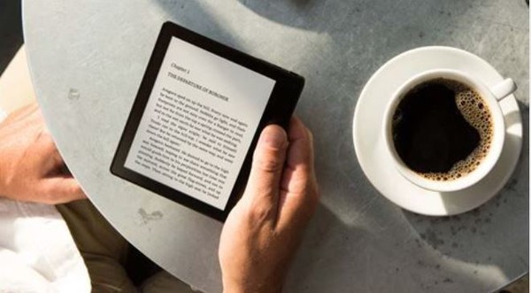 Hand holding kindle with a cup of coffee