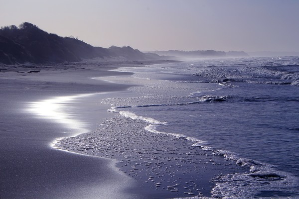 Atmospheric picture of waves lapping against the san with a mountain in the distance