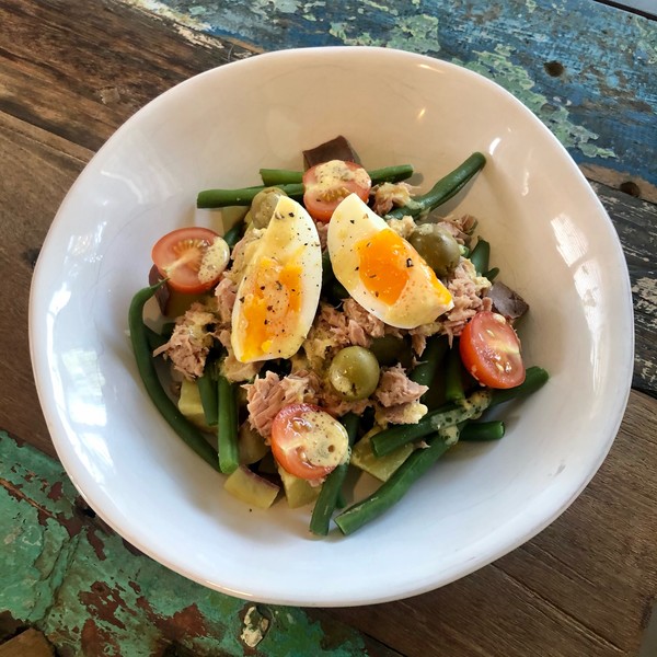 A white bowl of nicoise salad with egg, beans, tomatoes